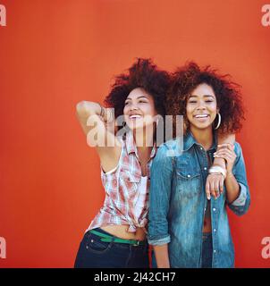 Beste Freunde machen die glücklichen Zeiten noch glücklicher. Aufnahme von zwei jungen Freunden, die vor einem roten Hintergrund posieren. Stockfoto