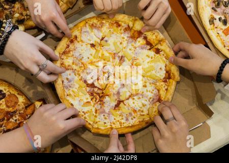 Draufsicht, viele Freunde, Hände, die nach einem Stück Pizza auf dem Tisch greifen Stockfoto