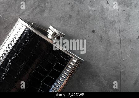 Taschenflasche aus Stahl in Lederoptik mit einem alkoholischen Getränk auf dunklem Hintergrund mit Kopierfläche Stockfoto