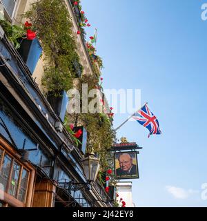 London, Großbritannien - 24. März 2022: Das Äußere des Churchill Arms Pubs in Kensington, London. Die Fassade ist mit roten Tulpen und einem Union Jack Fla dekoriert Stockfoto