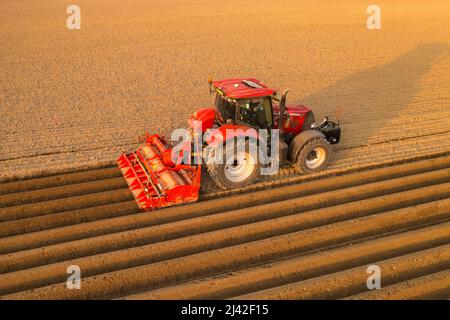 PRAG , TSCHECHISCHE REPUBLIK - MÄRZ 18 2022: Schwerer Traktor bereitet Bodenbeete für die Pflanzung auf dem ländlichen Feld vor. Landwirtschaftliche Maschine arbeitet bei Sonnenuntergang in Landschaft Luftaufnahme Stockfoto