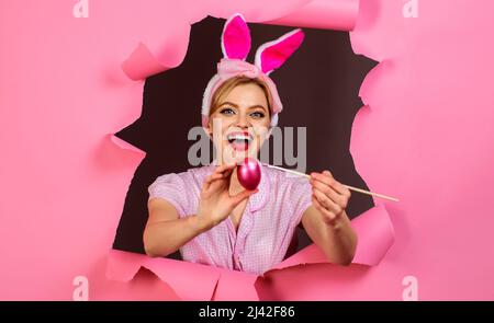 Glückliche Frau in gefälschten Hasenohren malen osterei. Kaninchen Mädchen mit Pinsel und rosa Ei. Stockfoto