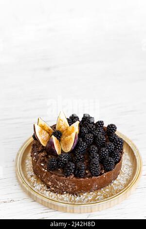 Roher, veganer, reicher dunkler Schokoladenkuchen auf einem weißen Tisch. Minimalismus Food Fotografie Konzept. Der Kuchen ist mit Brombeeren und gerösteter Feige verziert. SPA kopieren Stockfoto