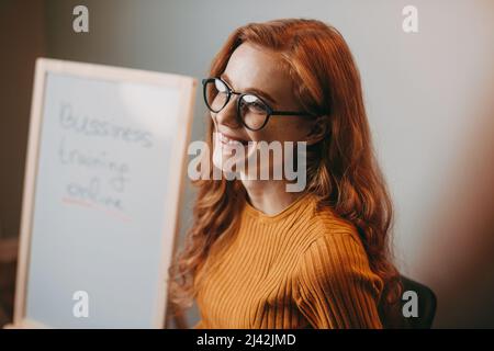 Porträt einer kaukasischen lächelnden rotköpfigen Frau, die eine Brille trägt und wegschaut. Porträt einer Geschäftsfrau. Unternehmensporträt. Business Intelligence. Stockfoto