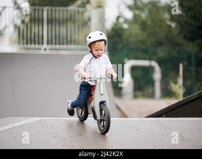 Kind reitet Laufrad. Männliches Kleinkind im Helm, das im Skatepark lernt, auf dem Laufrad zu fahren. Stockfoto