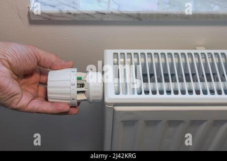 Nahaufnahme der Hand einer Person, die den Thermostat am Heizkörper abschaltet, um Energie zu sparen. Schweden. Stockfoto