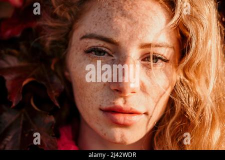 Nahaufnahme einer schönen jungen kaukasischen Frau mit lockig blondem Haar und Sommersprossen, die die Kamera anschaut und lächelt. Niedliche Frau Porträt in einem rosa lang Stockfoto