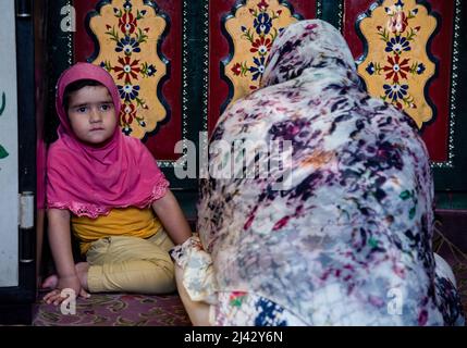 Srinagar, Indien. 11. April 2022. Ein muslimisches Mädchen schaut zu, während sie während des islamischen heiligen Monats Ramadan neben ihrer Mutter in einem Schrein sitzt. Der heiligste Monat des Islam Ramadan ist eine Zeit des intensiven Gebets, des Fastens von Sonnenaufgang bis Sonnenuntergang und der nächtlichen Feste. Kredit: SOPA Images Limited/Alamy Live Nachrichten Stockfoto