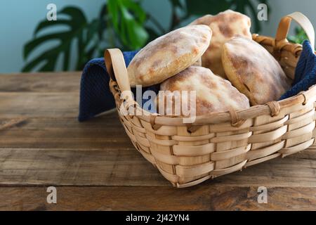 Holzkorb mit mehreren Stücken hausgemachtem Pita-Brot auf Holztisch. Speicherplatz kopieren. Stockfoto