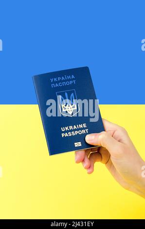 Ukrainischer Pass in der Hand einer Frau vor dem Hintergrund der ukrainischen Flagge Stockfoto