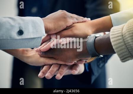 Wir können alles erreichen. Aufnahme von Geschäftskollegen mit gestapelten Händen bei der Arbeit. Stockfoto