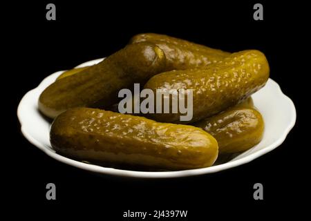 Gesalzene, eingelegte Gurken auf einem weißen Teller auf schwarzem Grund Stockfoto