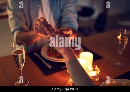 Der perfekte Anlass. Kurzer Schuss eines unkenntlichen Mannes, der seiner Frau bei einem nächtlichen Candle-Light-Dinner vorschlug. Stockfoto