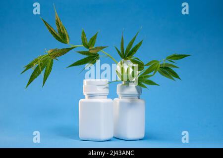 Zwei weiße Gläser und Cannabisblätter auf blauem Hintergrund. Stockfoto