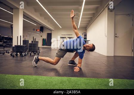 Entschlossen, seine Fitnessziele zu erreichen. Ganzkörperaufnahme eines hübschen jungen Mannes, der sich beim Training im Fitnessstudio dehnt. Stockfoto