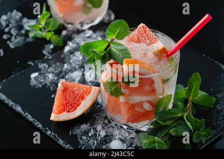 Erfrischender Grapefruit-Cocktail mit Eis und Minze auf schwarzem Hintergrund Stockfoto