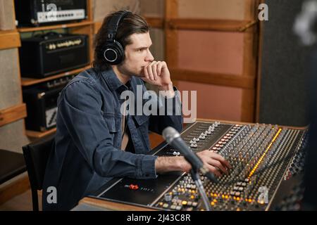 Seitenansicht Porträt eines fokussierten jungen Mannes, der Kopfhörer an einem Audio-Arbeitsplatz in einem professionellen Aufnahmestudio, in der Musikproduktion und in der Artistik trägt Stockfoto