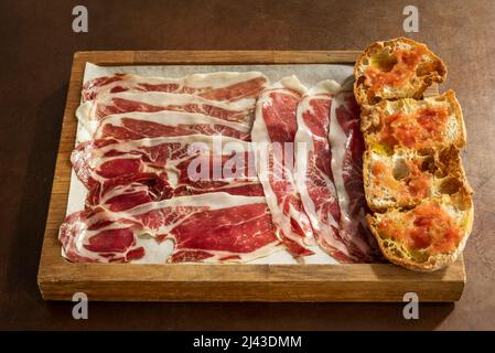 Holzschale mit Scheiben Jabugo-Schinken und gehacktem Toast mit Olivenöl und zerkleinerten Tomaten Stockfoto