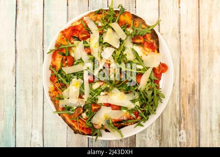 Bild von oben: Pizza mit viel Rucola, Parmesan-Flocken, Tomatensauce und Kirschtomaten mit Olivenöl Stockfoto
