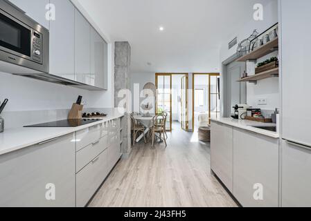 Offene Küche mit hellen Holzmöbeln kombiniert mit weißen Stein Arbeitsplatte und Geräte, Esszimmer mit runden Holztisch und Fenster in der Stockfoto