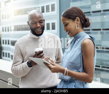 Überwachung von Trends, die sich täglich ändern. Aufnahme von zwei Geschäftsleuten, die vor einem Büro ein digitales Tablet benutzen. Stockfoto