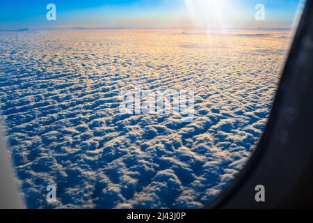 Blick vom Flugzeugfenster auf die aufgehende Sonne über der Wolkendecke (Kopierraum) Stockfoto