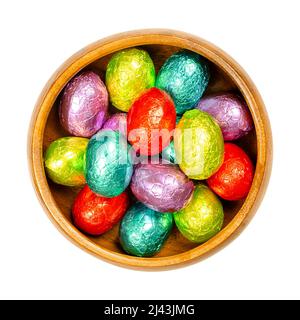 Gemischte farbige, in Folie gewickelte Schokoladen-Ostereier in einer Holzschale. Mini-Schokolade Eier, süße Süßigkeiten, in Aluminiumfolie in verschiedenen Farben gewickelt. Stockfoto