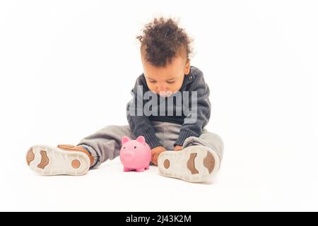 Schöne afroamerikanische gewellten kleinen Jungen auf dem Boden sitzen Blick auf die rosa Spielzeug Schwein Studio Schuss weißen Hintergrund voller Schuss Kopie Raum . Hochwertige Fotos Stockfoto