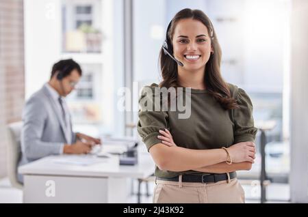 Bereitstellung eines exzellenten Kundendienstes. Porträt einer jungen Callcenter-Agentin, die mit gekreuzten Armen in einem Büro mit ihrer Kollegin im steht Stockfoto