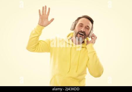 Fröhlicher, reifer Mann hört Musik oder Hörbücher in Kopfhörern, die auf weißer, drahtloser Technologie isoliert sind. Stockfoto