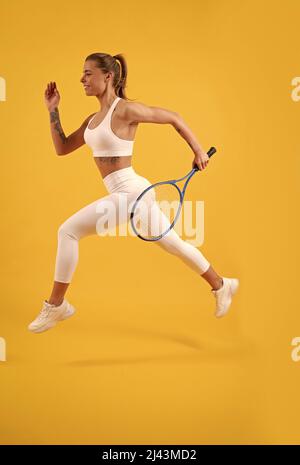 Glücklicher Tennisspieler läuft mit Schläger auf gelbem Hintergrund, Badminton Stockfoto