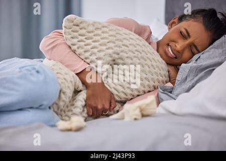 Es ist wieder die Zeit des Monats. Kurzer Schuss einer attraktiven jungen Frau, die zu Hause auf ihrem Bett liegt, während sie an Menstruationskrämpfen leidet. Stockfoto