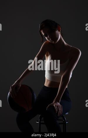 Teenager Mädchen mit Basketball. Seitlich beleuchtetes Studioporträt vor dunklem Hintergrund. Stockfoto