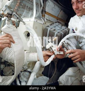 Eine Innenansicht der Apollo 13 Mondlandefähre (LM) während der von den Schwierigkeiten geplagten Reise zurück zur Erde. Dieses Foto zeigt einige der provisorischen Schlauchanschlüsse und Geräte, die notwendig waren, als die drei Apollo-Astronauten vom Command Module (CM) zur Verwendung des LM als „Rettungsboot“ umzogen. Astronaut John L. Swigert Jr., Kommandomodulpilot, befindet sich auf der rechten Seite. Ein unbesehbarer Lovell auf der linken Seite hält in seiner rechten Hand den Futterwasserbeutel des tragbaren Lebenserstützungssystems (PLSS). Er ist mit einem Schlauch (Mitte) der topografischen Mondkamera (HyCon) verbunden. Im Hintergrund befindet sich die „Mitschachtel“, Stockfoto