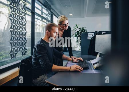 Geschäftsmann, der an einem Computer arbeitet, und der Manager steht bereit. Kollegen, die im Büro arbeiten. Stockfoto