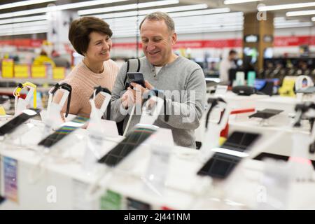 Ehefrau und Ehemann mittleren Alters pflücken neues Smartphone im Elektronikgeschäft Stockfoto