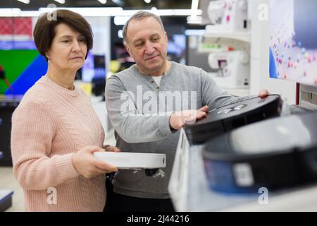 Europäische Ehegatten im reifen Alter entscheiden sich für einen Roboter-Staubsauger Stockfoto