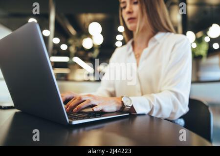 Geschäftsfrau, die auf einem Laptop auf der Arbeit schreibt. Zielgerichtete junge Geschäftsfrau, die einen Laptop benutzt, während sie an einem modernen Arbeitsplatz arbeitet. Unternehmerin sitzend Stockfoto