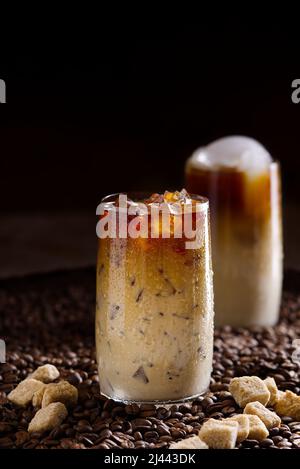 Eiskaffee. Leckerer Eiskaffee mit Milch, kaltes Getränk im Glas mit Eis auf dunklem Kaffeehintergrund. Stockfoto