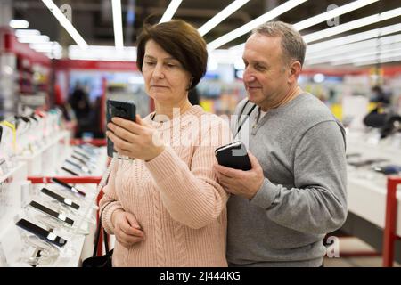 Seniorenpaar, das sich im Technikgeschäft für ein Smartphone entschieden hat Stockfoto