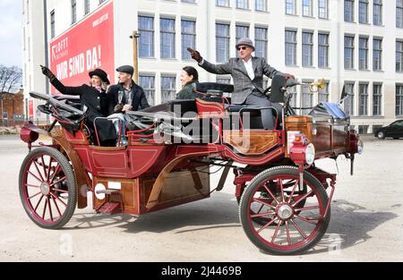 PRODUKTION - 03. April 2022, Sachsen, Leipzig: In einer Tweed-Jacke und einem grauen Melone chauffiert der ehemalige Automanager Joe Laube in seinem historisch anmutenden E-Wagen durch das Leipziger Industriegebiet. Als Touristenattraktion kann er in seiner komfortablen Kutsche ohne Pferde bis zu sieben Personen unterbringen, denen je nach Wunsch verschiedene Touren zu Sehenswürdigkeiten in der Stadt und Umgebung angeboten werden. Mit einer Höchstgeschwindigkeit von 25 Stundenkilometern und dem leisen Schnurren des Elektromotors können seine Gäste dann die ungewöhnliche Fahrt bei einem Glas Champagner, Musik und Geschichten genießen. (Bis dpa Stockfoto