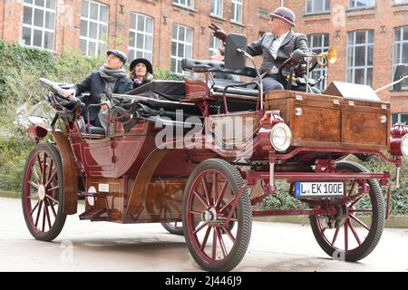 PRODUKTION - 03. April 2022, Sachsen, Leipzig: In einer Tweed-Jacke und einem grauen Melone chauffiert der ehemalige Automanager Joe Laube in seinem historisch anmutenden E-Wagen durch das Leipziger Industriegebiet. Als Touristenattraktion kann er in seiner komfortablen Kutsche ohne Pferde bis zu sieben Personen unterbringen, denen je nach Wunsch verschiedene Touren zu Sehenswürdigkeiten in der Stadt und Umgebung angeboten werden. Mit einer Höchstgeschwindigkeit von 25 Stundenkilometern und dem leisen Schnurren des Elektromotors können seine Gäste dann die ungewöhnliche Fahrt bei einem Glas Champagner, Musik und Geschichten genießen. (Bis dpa Stockfoto