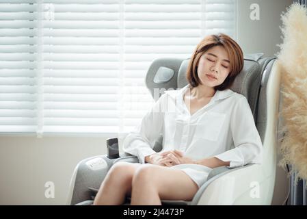 Eine Frau entspannt sich auf ihrem Massagesessel im Wohnzimmer beim Nickerchen. Stockfoto