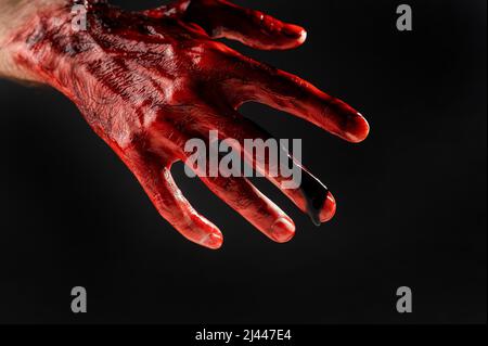 Nahaufnahme einer mit Blut befleckten männlichen Hand auf schwarzem Hintergrund. Stockfoto