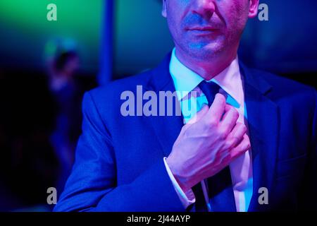 Erfolgreich, aber zwielichtig. Aufnahme eines zwielichtigen Geschäftsmannes, der seine Krawatte in einer Go-Bar anpasst, mit einer Frau, die auf einer Stange hinter ihm tanzt. Stockfoto