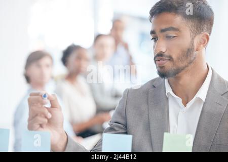 HES hat die perfekte Idee. Aufnahme eines jungen Geschäftsmannes, der bei der Arbeit auf einer transparenten Tafel schreibt. Stockfoto