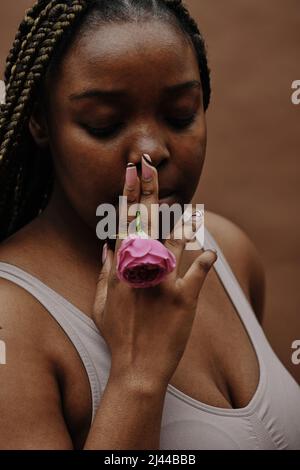 Afrikanische junge Frau mit Zöpfen, die rosa Rose im Mund halten und sie als Zigarette rauchen Stockfoto