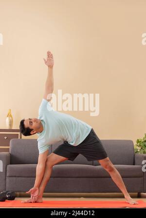 Porträt eines jungen Mannes, der zu Hause auf einer Trainingsmatte Yoga macht Stockfoto