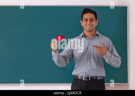 Die Lehrerin zeigt auf die Kreditkarte, während sie vor der Tafel im Klassenzimmer steht Stockfoto