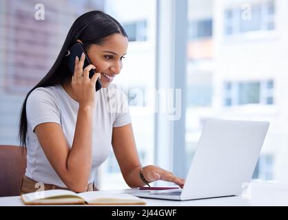 Klar, ich schaue mir das jetzt an. Eine kurze Aufnahme einer attraktiven jungen Geschäftsfrau, die während der Arbeit am Laptop im Büro einen Anruf macht. Stockfoto